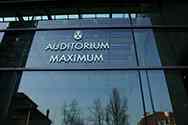 Logo en acier inoxydable de l'Auditorium Maximum sur cloison de verre montée avec un système en inox.